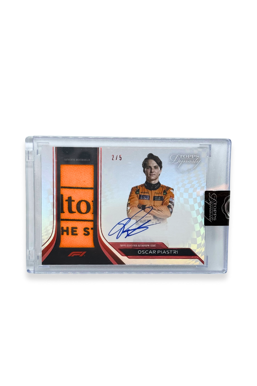 Front of 2024 Topps Dynasty Oscar Piastri patch autograph card, serial numbered 2 of 5, featuring orange and black memorabilia with partial lettering from Hilton’s “For The Stay” logo.
